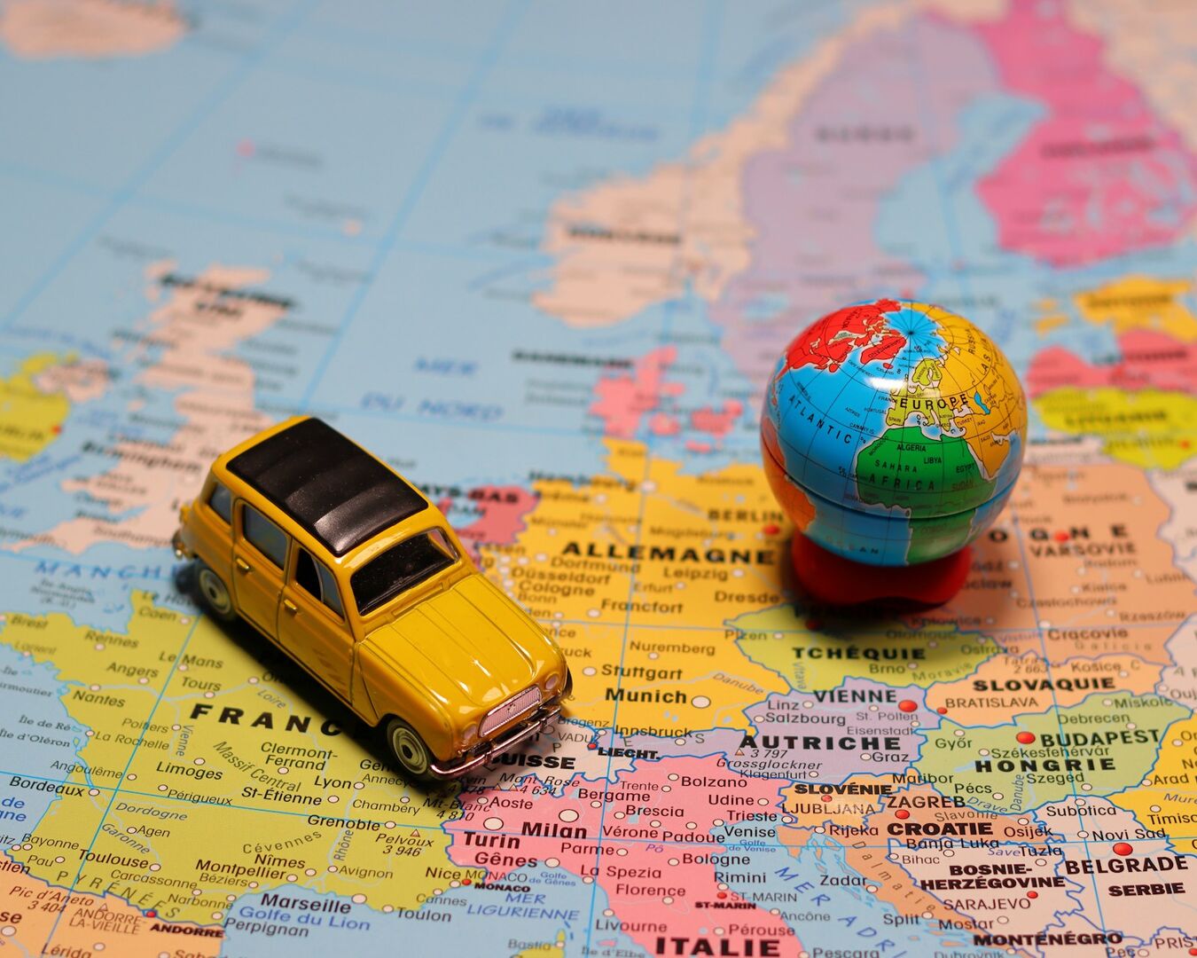 Gelbes Spielzeugauto steht auf einer Landkarte Europas, daneben eine kleine Weltkugel.