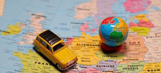Gelbes Spielzeugauto steht auf einer Landkarte Europas, daneben eine kleine Weltkugel.