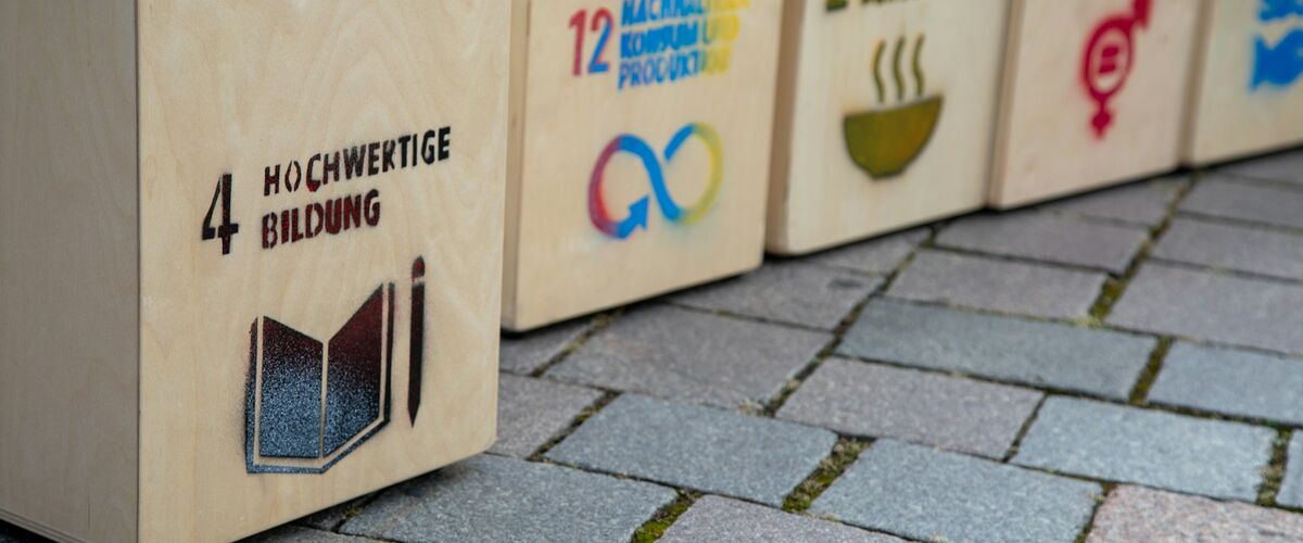 Holzkisten auf Bürgersteig mit Aufdruck SDGs / Ziele für nachhaltige Entwicklung