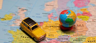 Gelbes Spielzeugauto steht auf einer Landkarte Europas, daneben eine kleine Weltkugel.