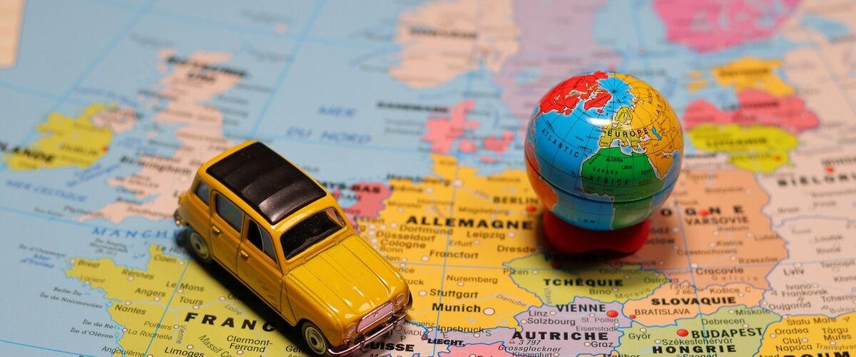 Gelbes Spielzeugauto steht auf einer Landkarte Europas, daneben eine kleine Weltkugel.
